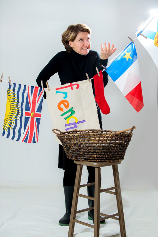 A woman stands behind clothesline of colourful flags. She grimaces. A stool with a basket is in the foreground. 